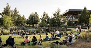people sitting on a lawn in front of a massive building surrounded by other people